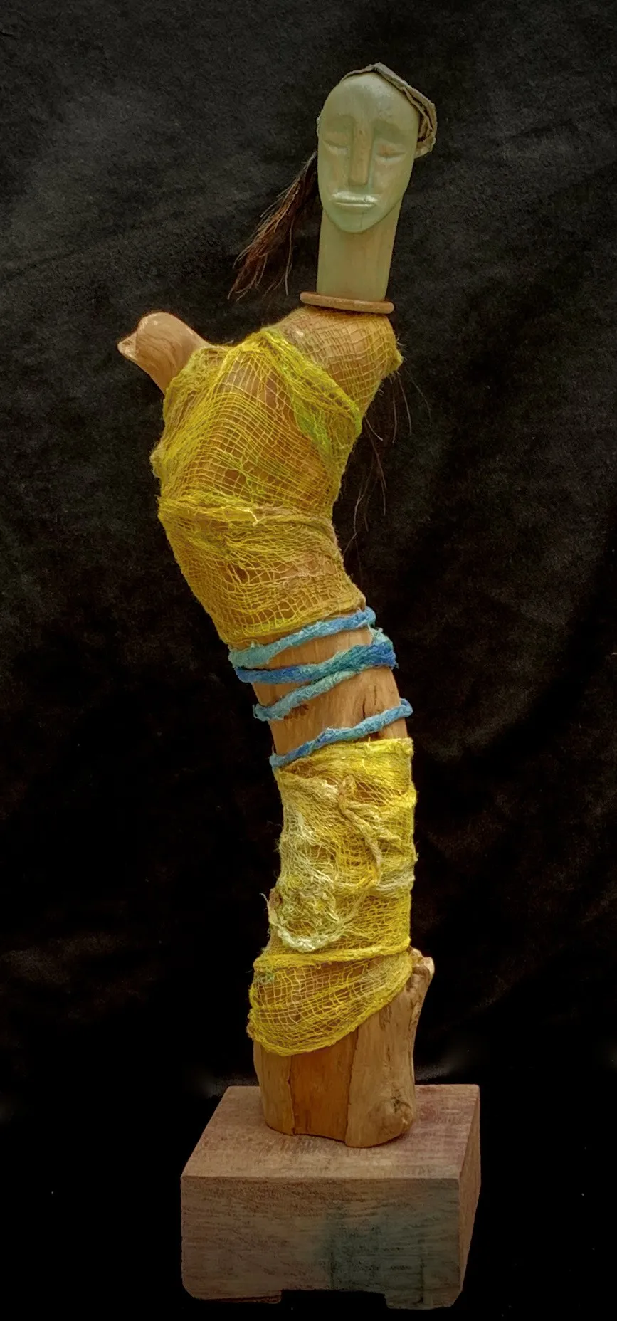 A wooden sculpture adorned with a bright yellow scarf
