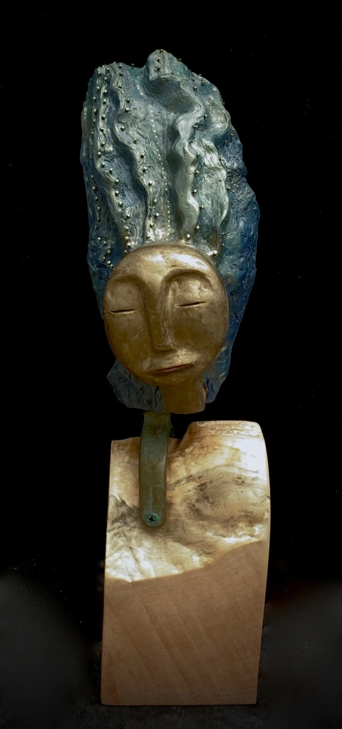 A sculpture of a woman with blue hair displayed on a wooden block
